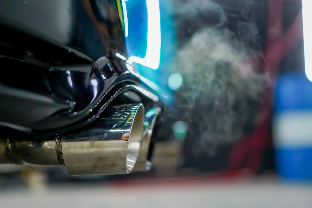 Close-up of the exhaust pipe emitting smoke from a chameleon-colored luxury car in the process of car washing